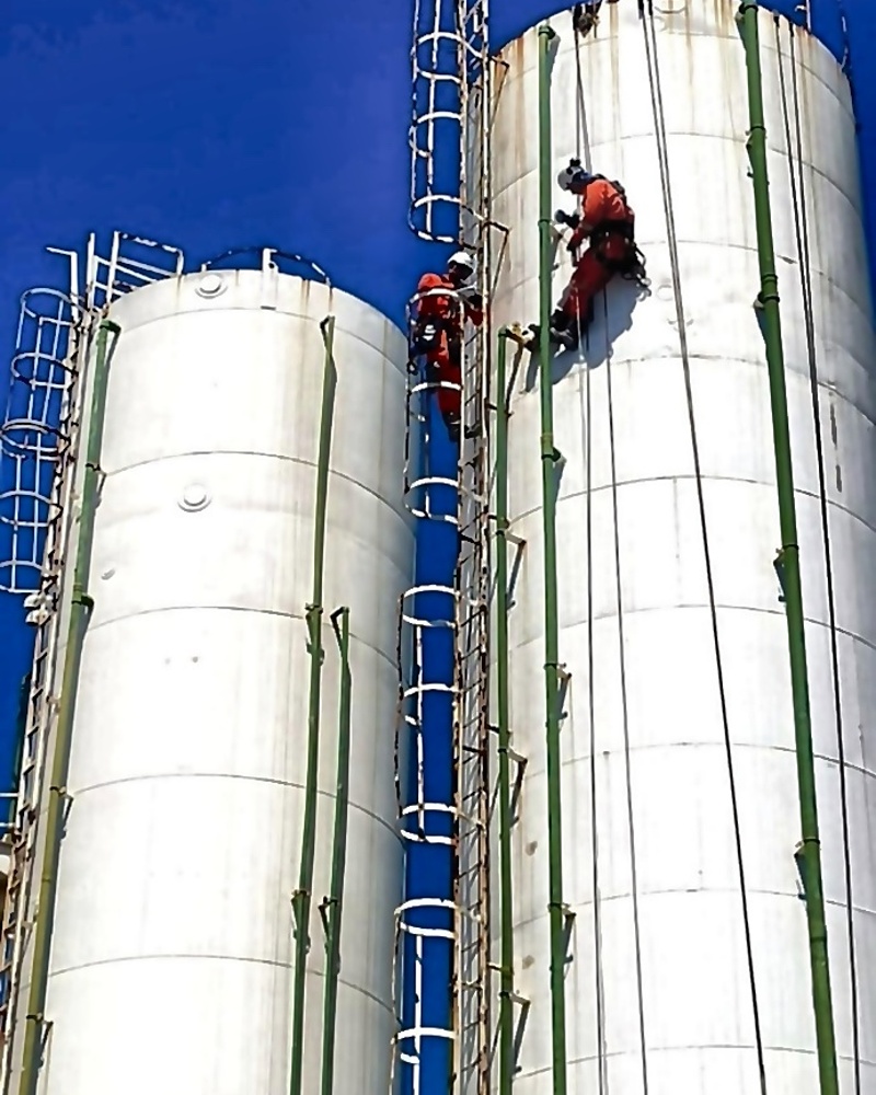 Dupla de técnicos em escalada industrial em silos verticais sob céu aberto