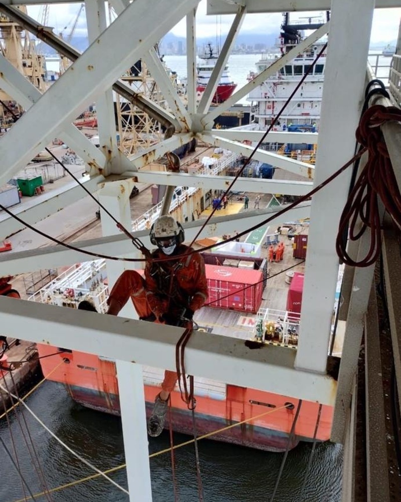 Técnico suspenso em estrutura metálica sobre cais portuário